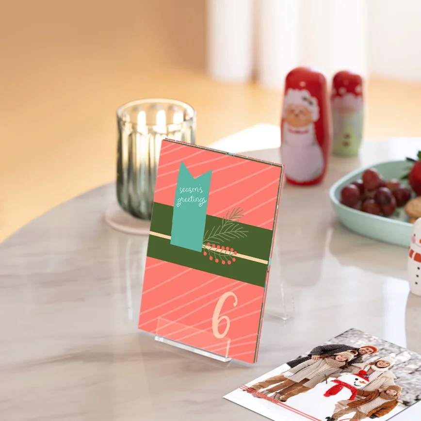 Advent calendar with stand: Twelve rectangular photo prints with decorative scalloped edges in various pastel colors, fanned out against a dark green background, each featuring a family photo.