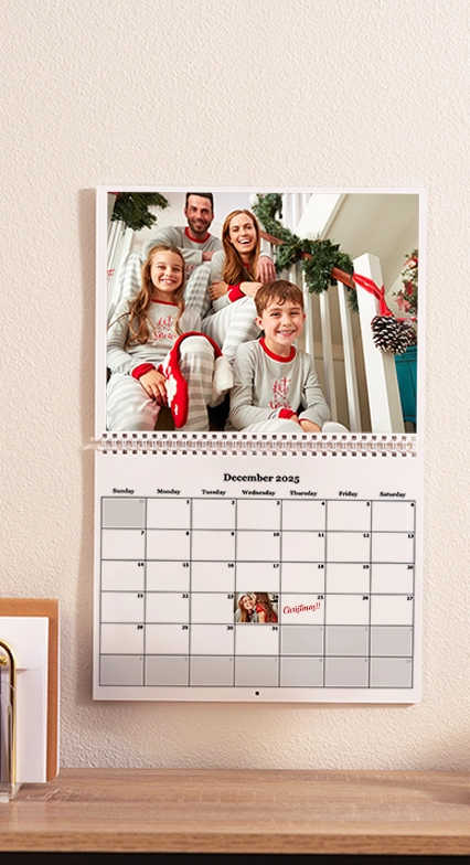 Custom Desktop Calendars: A wall calendar for December 2025 hanging above a desk, featuring a photo of a family of four smiling in matching pajamas.